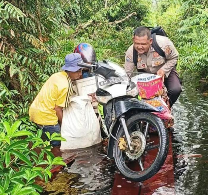 Bhabinkamtibmas di Tebingtinggi Timur Ini Bantu Warga Melintasi Jalan Terendam Banjir